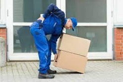 Person bent over wearing blue holding their lower back in pain while also holding boxes.